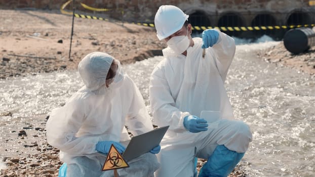 Biologist wear protective suit and mask collects sample of waste water from industry, problem environment, Ecologist sample taken dead fish to inspection and save data to laptop computer, Toxic water