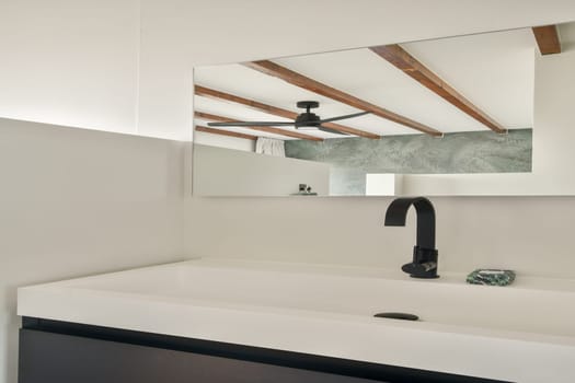 A contemporary bathroom featuring a sleek sink and a large mirror, showcasing intricate ceiling beams and a textured wall design for an elegant ambiance.