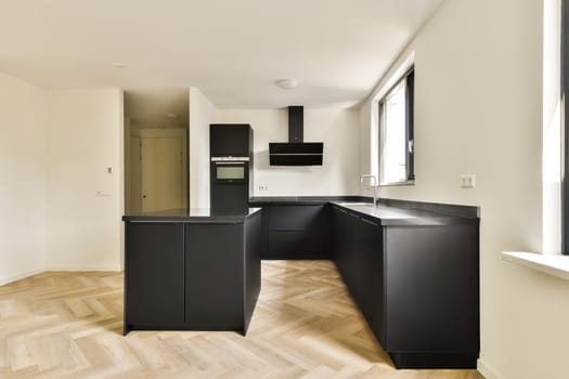 A sleek and contemporary kitchen featuring minimalist design, dark cabinetry, and elegant flooring. The space embraces an open layout with natural light streaming in.