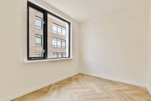 Bright, spacious interior showcasing a large window, providing a view of the outside. The minimalist design features light-colored walls and herringbone flooring.