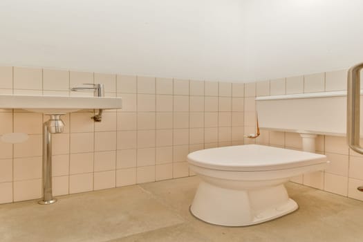 A clean and minimalistic design featuring beige tiles and simple fixtures, highlighting a toilet and sink in a spacious layout.