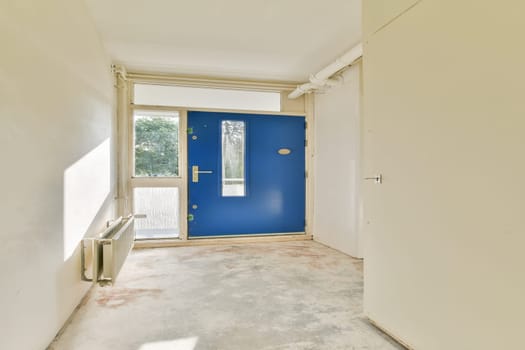 An inviting entrance showcasing a bright blue door against a minimalistic interior design. Sunlight filters in, highlighting the simplicity of the space.