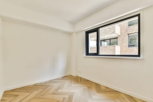 A spacious modern room featuring large windows that allow natural light to flood in. The wooden flooring adds warmth to the minimalist design.