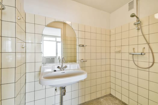 A sleek and minimalist bathroom featuring white tiles, a simple sink with a modern faucet, and an oval mirror. The space conveys a clean and refreshing ambiance.