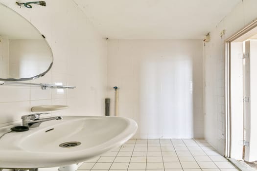 A minimalist modern bathroom featuring a white sink, mirror, and tiled floor. The light enhances the clean and spacious feel of the space.