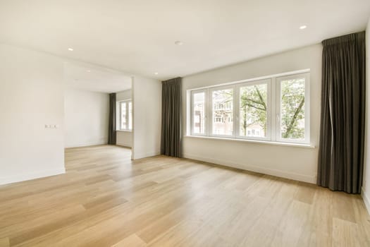 A bright and airy interior space featuring large windows and minimalist design. The floor is wooden, and the walls are painted in a soft, neutral tone.