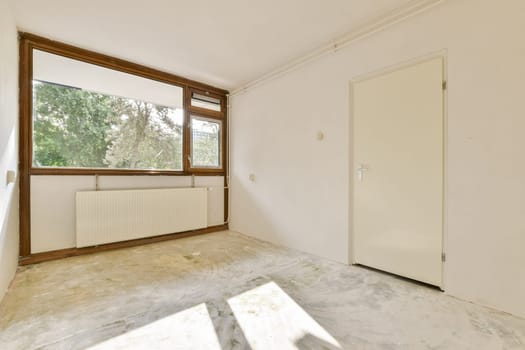 A bright, empty room featuring a large window that allows natural light to flood in, enhancing its spacious feel. The walls are plain, and the floor is unfinished.