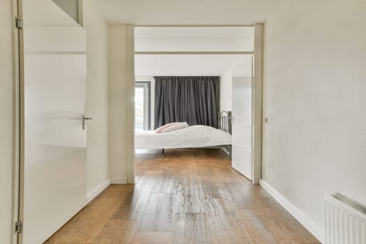 A bright, minimalist bedroom with neutral walls, wood flooring, and natural light flowing through sheer curtains. The calming atmosphere invites relaxation.