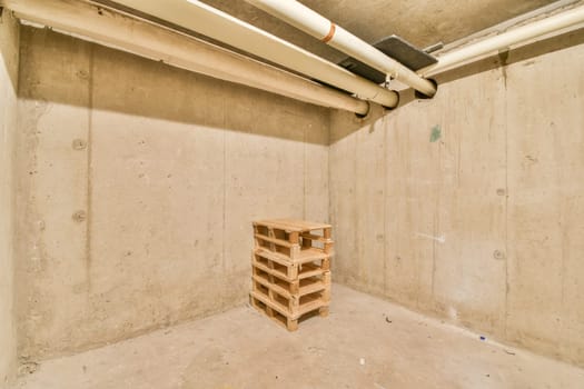An empty space featuring concrete walls and a wooden pallet positioned in the center, showcasing industrial elements and minimalist design.
