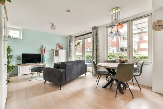 A stylish modern living room featuring a comfortable sofa, dining table, and large windows that provide natural light, showcasing contemporary furnishings and decor.
