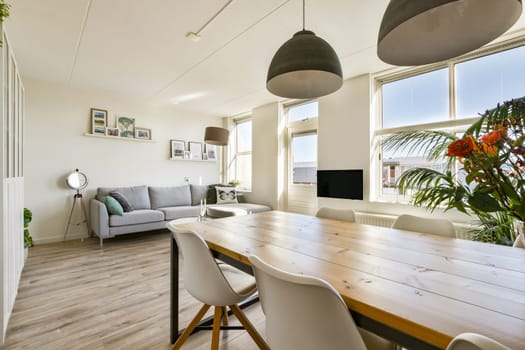 A stylish modern interior featuring a cozy seating area, a dining table, large windows for natural light, and decorative plants, creating a welcoming atmosphere.