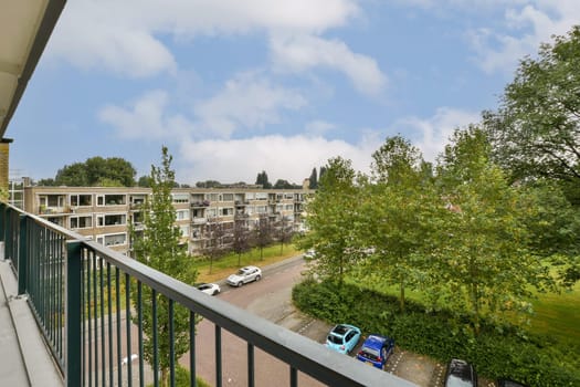A picturesque balcony view showcasing greenery, modern apartment buildings, and parked cars in a tranquil residential setting. A perfect blend of nature and urban life.