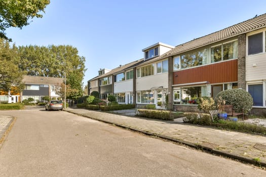 A picturesque suburban street featuring modern residential buildings, lush greenery, and parked cars under clear skies. Ideal for showcasing contemporary architecture.
