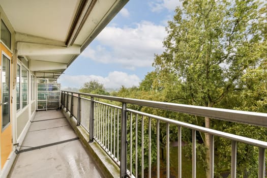A well-lit balcony features a sleek railing, overlooking vibrant green trees and clear skies, offering a peaceful outdoor retreat.