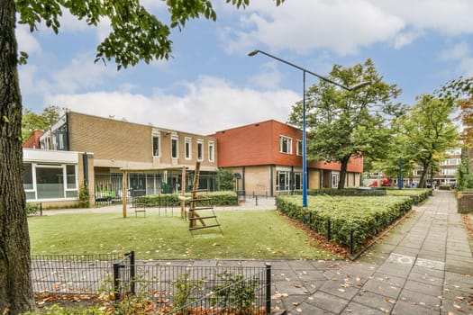 A serene view of a modern residential area featuring a playground amidst lush green grass and trees. The architecture blends well with the surroundings.