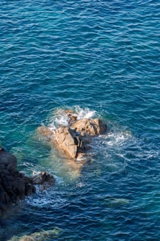 Wild rocky beach coastline and the sea, wave splashes on rock in sea shore, calm sea. Breaking waves to the rocks on shore creating white sea foam and small bubbles, top view