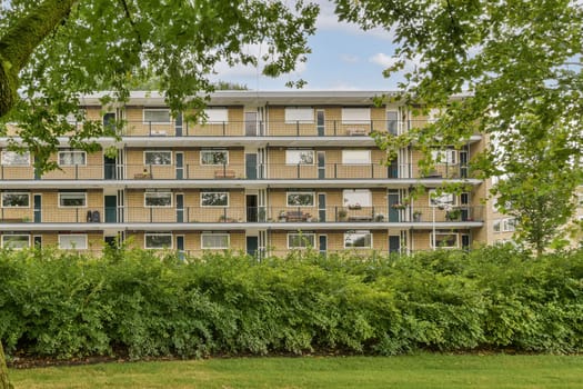 A contemporary residential building features multiple balconies and large windows, blending with lush greenery in the foreground, showcasing urban living.