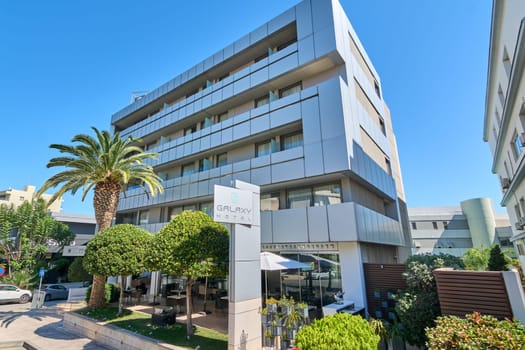 Crete.Greece - may 05, 2025: The contemporary facade of Galaxy Hotel, featuring sleek rectangular panels, large windows, and balconies surrounded by lush greenery under a bright blue sky.
