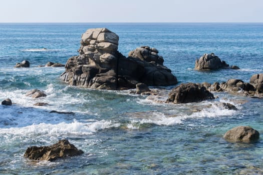 Wild rocky beach coastline and the sea, wave splashes on rock in sea shore, calm sea. Breaking waves to the rocks on shore creating white sea foam and small bubbles