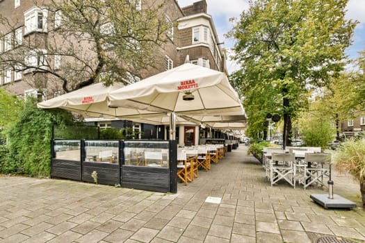 A beautifully arranged outdoor seating area with stylish furniture and shaded umbrellas, surrounded by greenery in an urban setting.