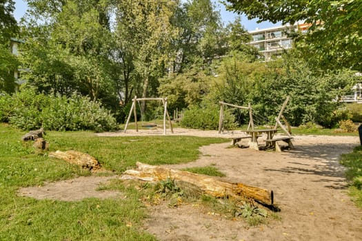A serene playground nestled in a lush park, surrounded by trees and greenery, featuring wooden swings and natural elements like logs on the ground.