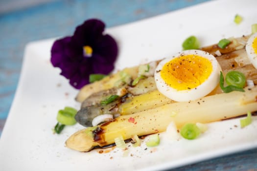 Baked asparagus with boiled egg in big white plate on blue background. High quality photo