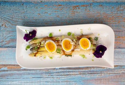 Baked asparagus with boiled egg in big white plate on blue background. High quality photo