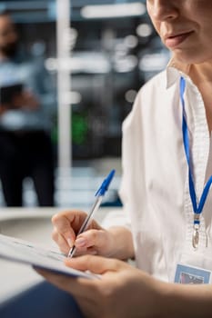Woman in data center taking note on fixes to be made after running diagnostic scripts on computer. Server room admin writing repairing needed by supercomputers after evaluating performance metrics