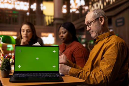 Focused group of university students read next to a green screen device, diverse people working on their thesis citations and documents. Analyzing coursework in a peaceful library.