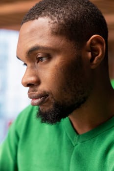 Close up side profile shot of young man with contemplative look doing tasks in apartment. African american person with focused expression looking at something, close up shot