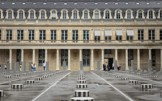 France, Paris - May 03, 2025 - Tourists enjoying of the Buren’s Columns (the two trays) installed in the Honor courtyard of the Palais Royal, A Contemporary Art is made of 260 black and white striped columns, All columns take root in the basement and emerge outdoor in different heights, creating a particular rhythm, and giving an unusual contrast with the classical architecture of the surrounding Palace. use it as your Wallpaper, Poster and Space for text, Selective focus.