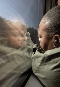 France, Paris - May 04, 2025 - Rear view of African-american female traveling by train and thinking while looking through train window. Reflection of a black women face looking out of the train's window, Concept about people and transportation, use it as your Wallpaper, Poster and Space for text, Selective focus.