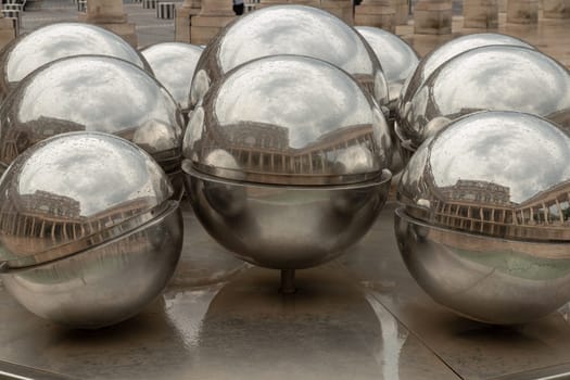 France, Paris - May 03, 2025 - View of 10 stainless steel spheres on Fontaines de Pol Bury (La Fontaine des Spheres) that slowly rotate on their axis, propelled by the flow of water cascading over them with reflecting the passersby in the court of Honor at the Palais-Royal. use it as your Wallpaper, Poster and Space for text, Selective focus.