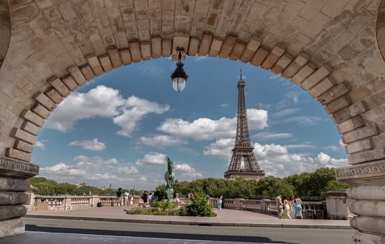 France, Paris - May 03, 2025 - Scenic view of the Eiffel tower in Paris with blue sky and cloud in the background, seen through an arch of a bridge with a brick structures in the center of Pont de Bir Hakeim. use it as your Wallpaper, Poster and Space for text, Selective focus.