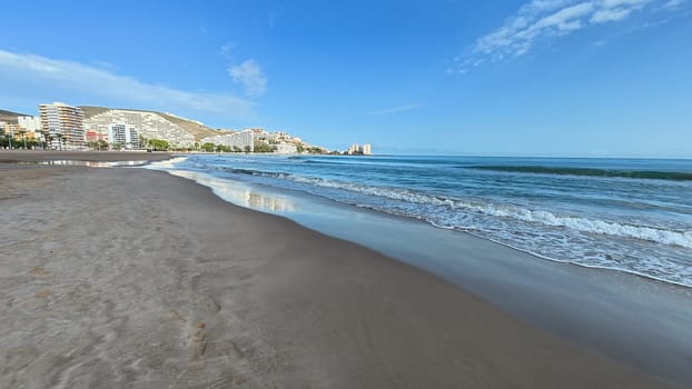 A serene beach view shows soft, golden sand, sunlit waves lapping, and a lovely, inviting coastline