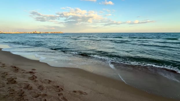 Immerse yourself in the serene beauty of gentle waves rolling onto the sandy shore during a vibrant sunset