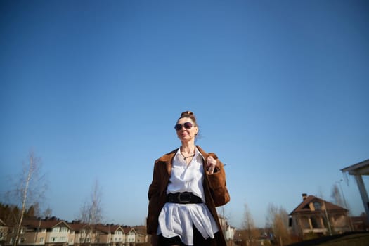 A fashionable woman strolls with confidence in a sunny urban setting, showcasing her unique style against the vivid blue sky.