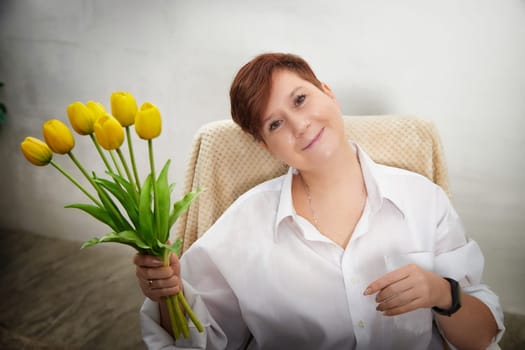 A middle-aged woman smiles while holding a bouquet of tulips in a warm and inviting space, celebrating Women's Day.