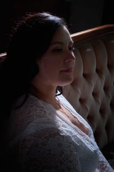 A plump woman gazes thoughtfully while dressed in a delicate lace outfit, capturing a moment of tranquility and elegance indoors.