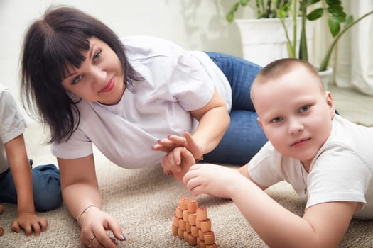 A woman and a boy are engaged in a stacking game with cups while two children play nearby, enjoying quality family bonding.