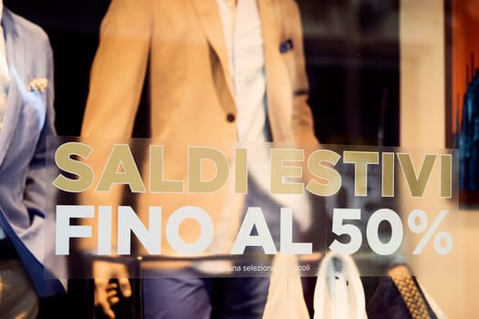 Milan, Italy - august 16, 2020 - Sale 50 off sticker on glass window display with mannequin in italian fashion store. Discount sign showcase of public cloth store for men.