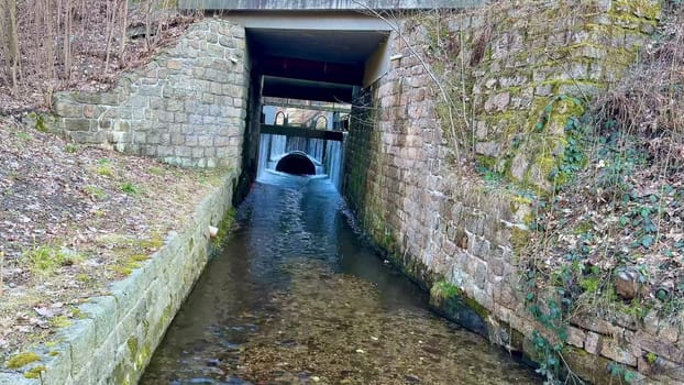 A beautifully tranquil view of a waterway gracefully flowing beneath a stunning stone archway in a lush forested area