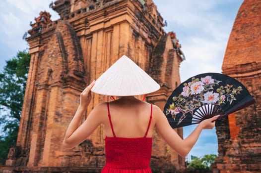 back of Asian girl tourist in Vietnamese cone hat with a fan on Cham Towers of Po Nagar in Nha Trang in Vietnam in Asia