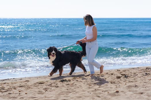 Woman on vacation walking her dog along the beach, barefoot on the sand, enjoying the ocean breeze and sunshine. Peaceful moment with a pet by the sea, feeling relaxed and carefree.