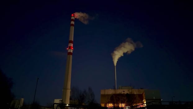 The captivating night view showcases smokestacks emitting both steam and smoke from an industrial facility