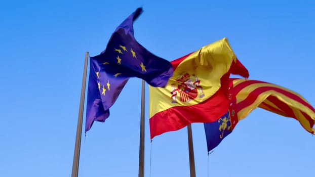 The European Union and Spanish national flags are waving proudly in the wind under a brilliantly bright blue sky