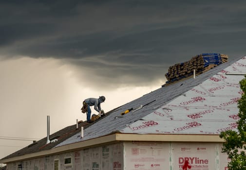 Georgetown, TX - 5 May 2025: Roofer installing shingles on roof of new home during thunderstorm and severe weather