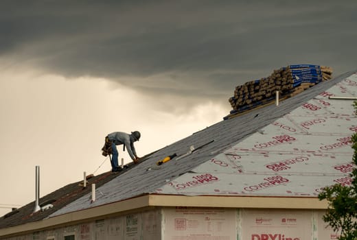 Georgetown, TX - 5 May 2025: Roofer installing shingles on roof of new home during thunderstorm and severe weather