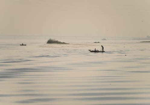Two men in their small boat on a calm river Nile while tending to fishing net in the water as dusk approaches