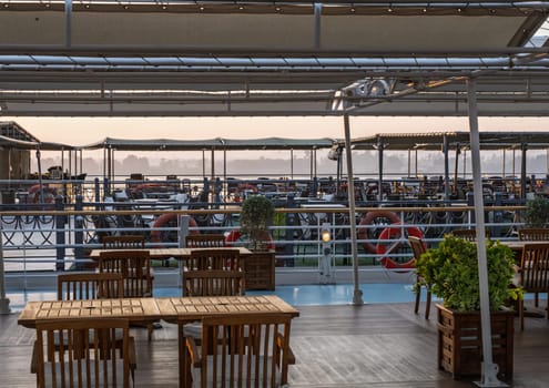 Sun rises over the tables and chairs on deck of Nile cruise boat docked alongside another ship in Edfu Egypt